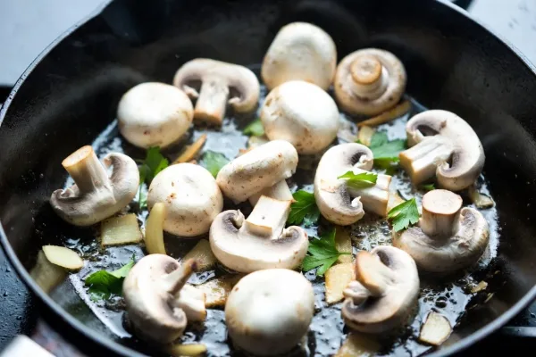 White button mushrooms browning in a skillet with garlic and parsley