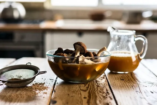Dried porcini mushrooms soaking in amber liquid beside a jug of strained mushroom broth