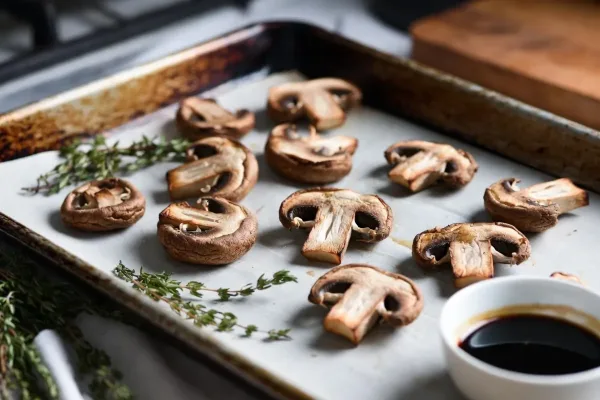 Halved cremini mushrooms roasted on a sheet pan with thyme and balsamic nearby