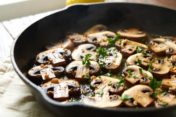 Golden-brown garlic-butter button mushrooms with parsley in a cast-iron skillet