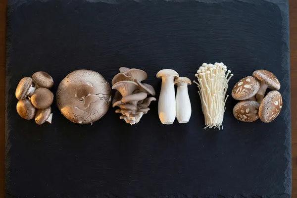 Cremini, oyster, shiitake, king oyster and enoki mushrooms arranged on a dark board