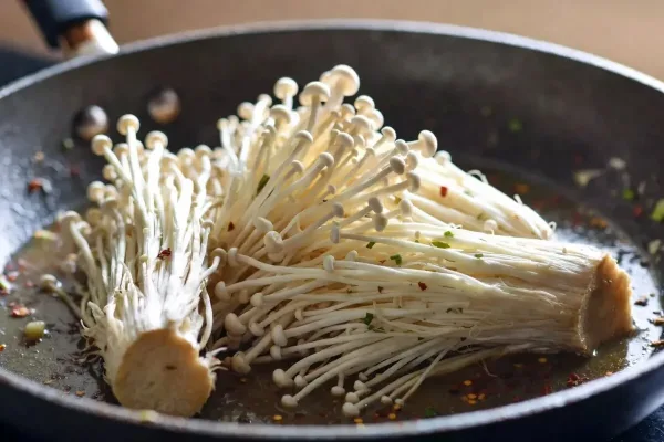 Garlic-butter enoki mushroom clusters with soy and scallions in a skillet