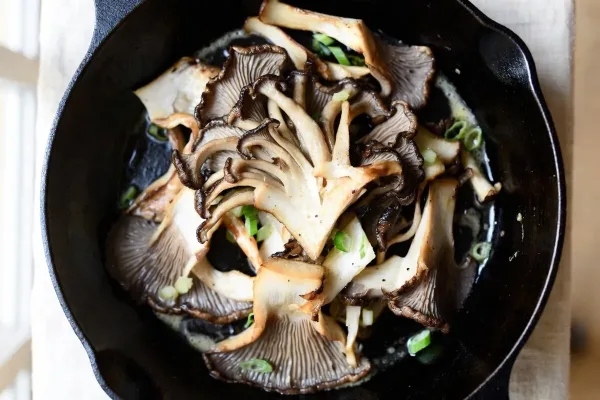 Golden-brown seared maitake mushrooms with crisp ruffled edges in a cast-iron skillet, garnished with garlic butter and scallions